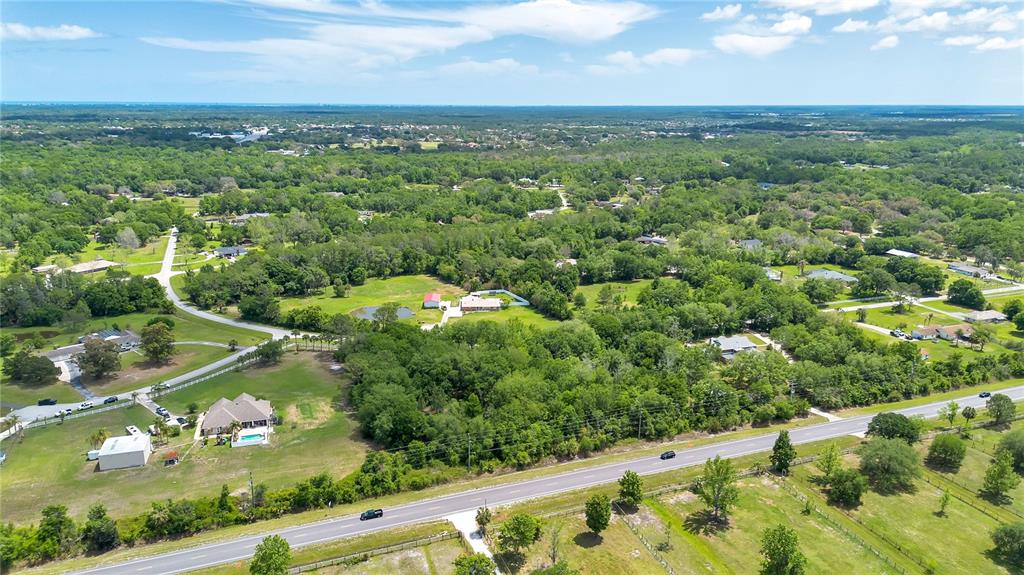 An aerial view shows a rural landscape with houses, a pond, and a paved road — 1903 SPRUCE CREEK CIRCLE, PORT ORANGE, FL