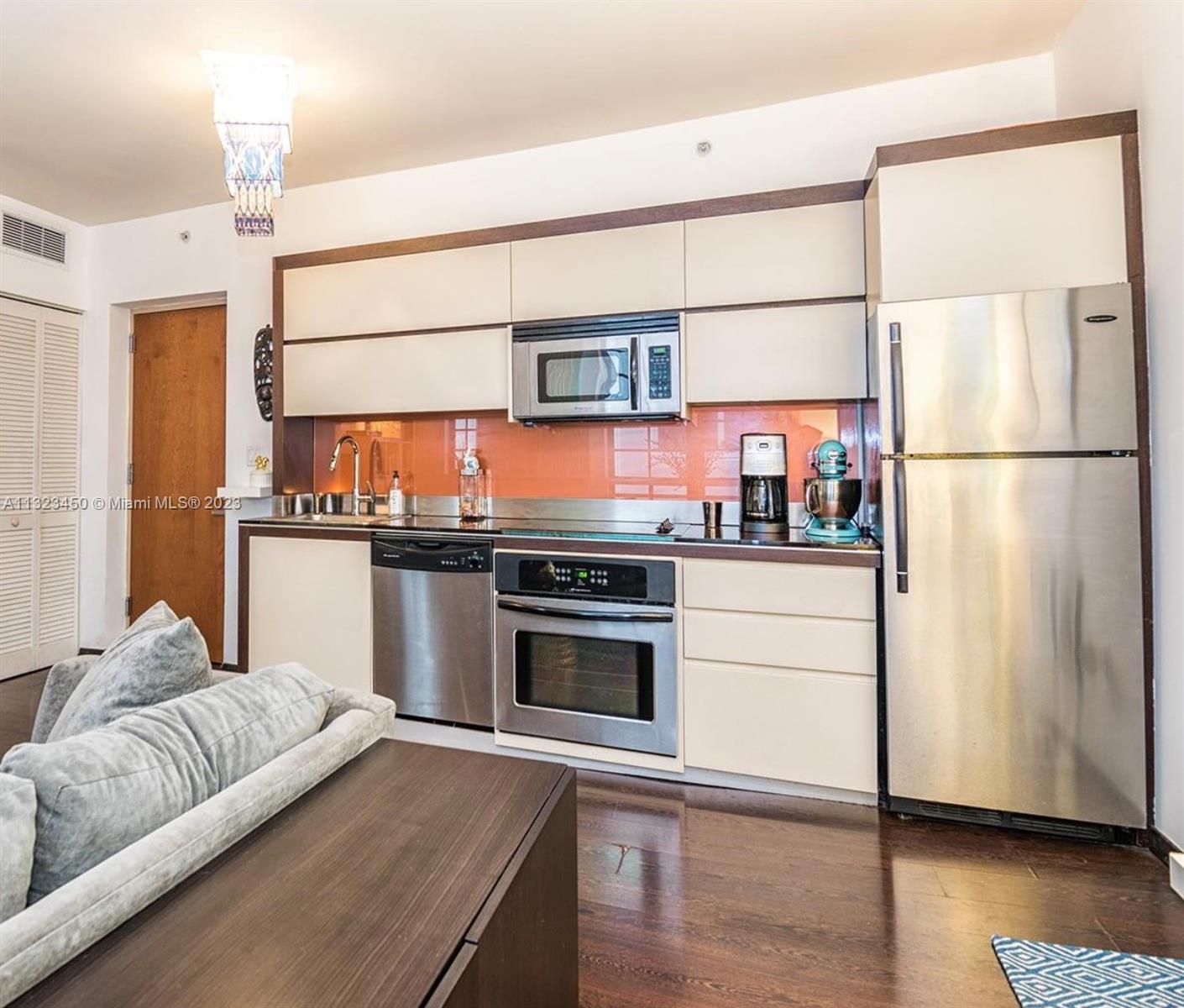 A kitchen features stainless steel appliances, light-colored cabinetry, and an orange glass backsplash — 435 21st St # 223, Miami Beach FL 33139, MIAMI BEACH, FL