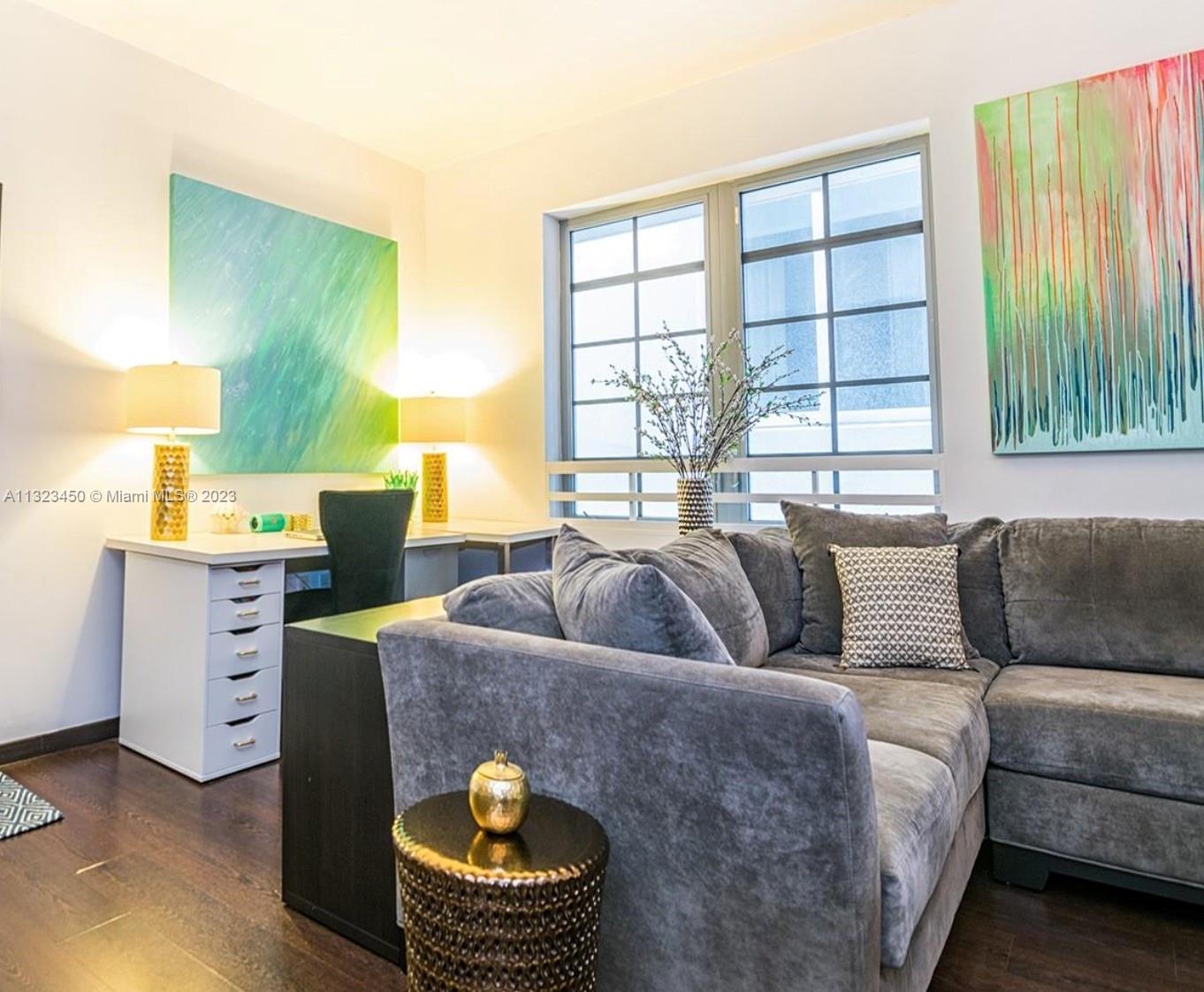 A room features a gray sectional sofa, a white desk with lamps, and abstract wall art — 435 21st St # 223, Miami Beach FL 33139, MIAMI BEACH, FL