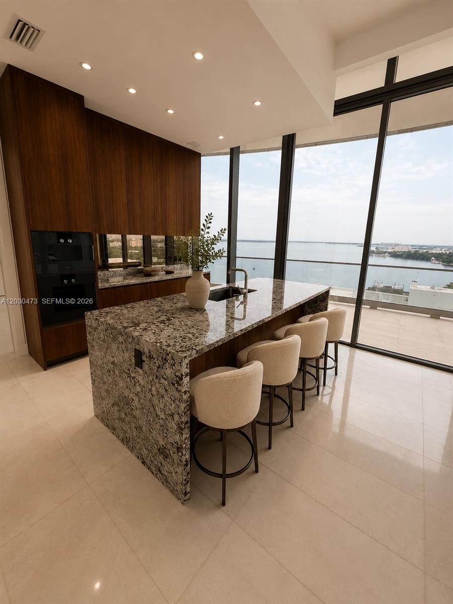 A modern kitchen features a granite island with bar seating and floor-to-ceiling windows overlooking water — 175 SE 25th rd # 1503, Miami FL 33129, MIAMI, FL