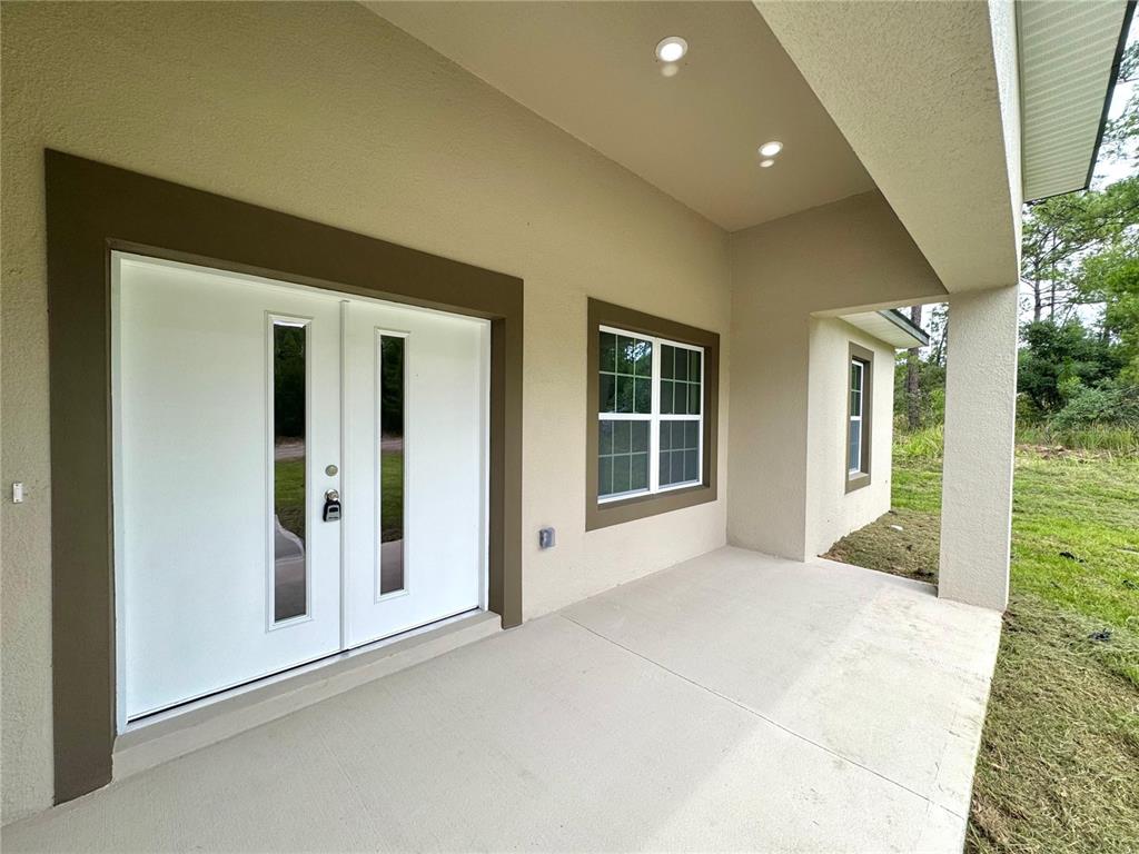 A covered concrete patio features double white doors with glass inserts and a window — 7222 N LIME DRIVE, CITRUS SPRINGS, FL