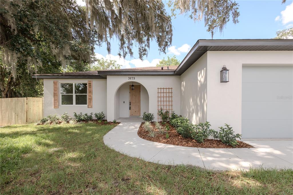 A single-story house with a white stucco exterior, arched entryway, and a light wood door — 3679 LINCOLN STREET, SANFORD, FL