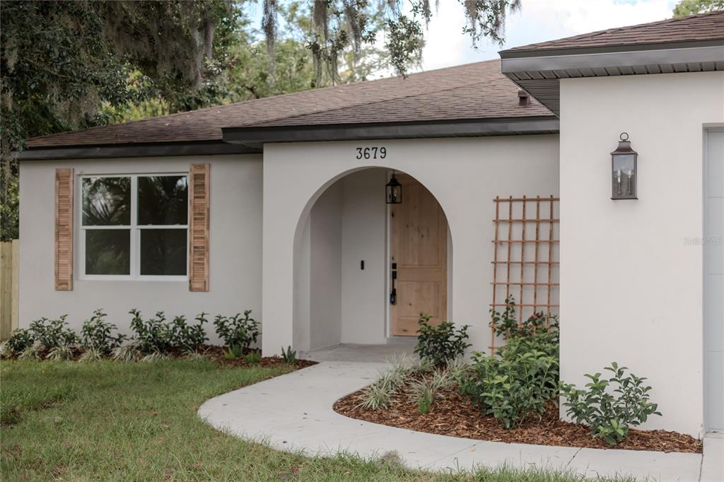 A single-story house exterior features a white stucco facade, arched entryway, and natural wood door — 3679 LINCOLN STREET, SANFORD, FL