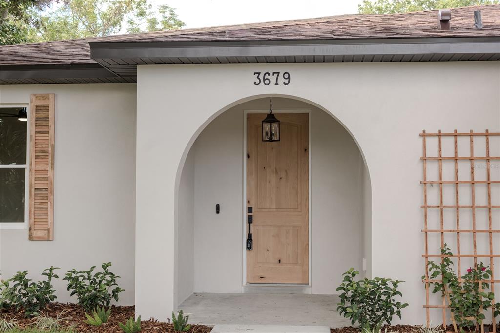 The exterior of a house features a light-colored arched entryway with a natural wood door — 3679 LINCOLN STREET, SANFORD, FL