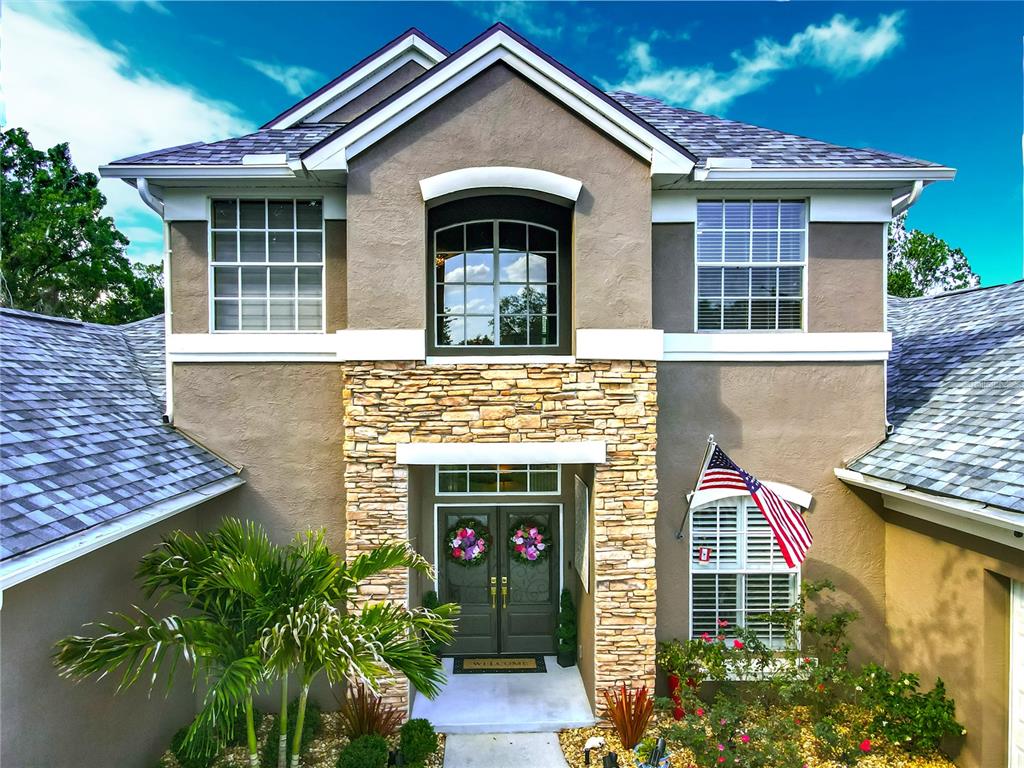 A two-story house exterior with a stone facade, double front doors, and an American flag — 3008 SUTTON WOODS DRIVE, PLANT CITY, FL