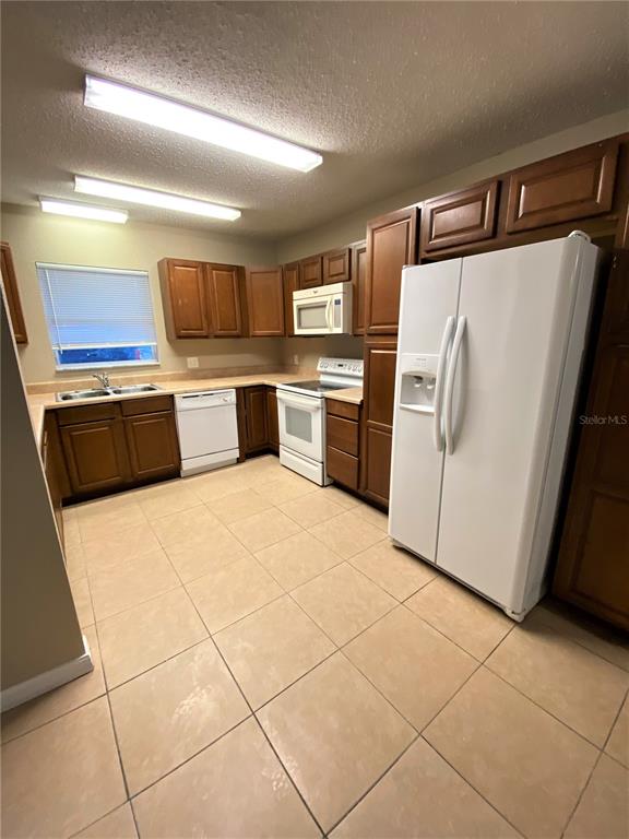 A kitchen features wood cabinets, white appliances, tile flooring, and two long ceiling lights — 2431 NW 4TH TERRACE UNIT 2431, GAINESVILLE, FL