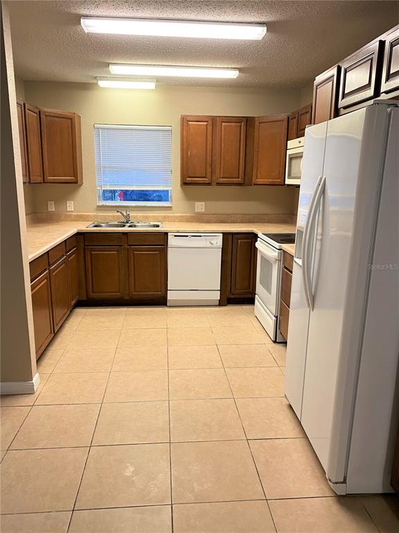 A kitchen with brown cabinets, white appliances, tile flooring, and a window above the sink — 2431 NW 4TH TERRACE UNIT 2431, GAINESVILLE, FL