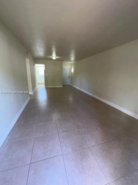 An empty room with beige walls and light-colored tile flooring leads toward a doorway — 7500 SW 82nd St # G110, Miami FL 33143, MIAMI, FL