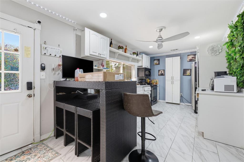A kitchen features white cabinets, a dark wicker bar with stools, and white tiled flooring — 2706 E ANNIE STREET, TAMPA, FL