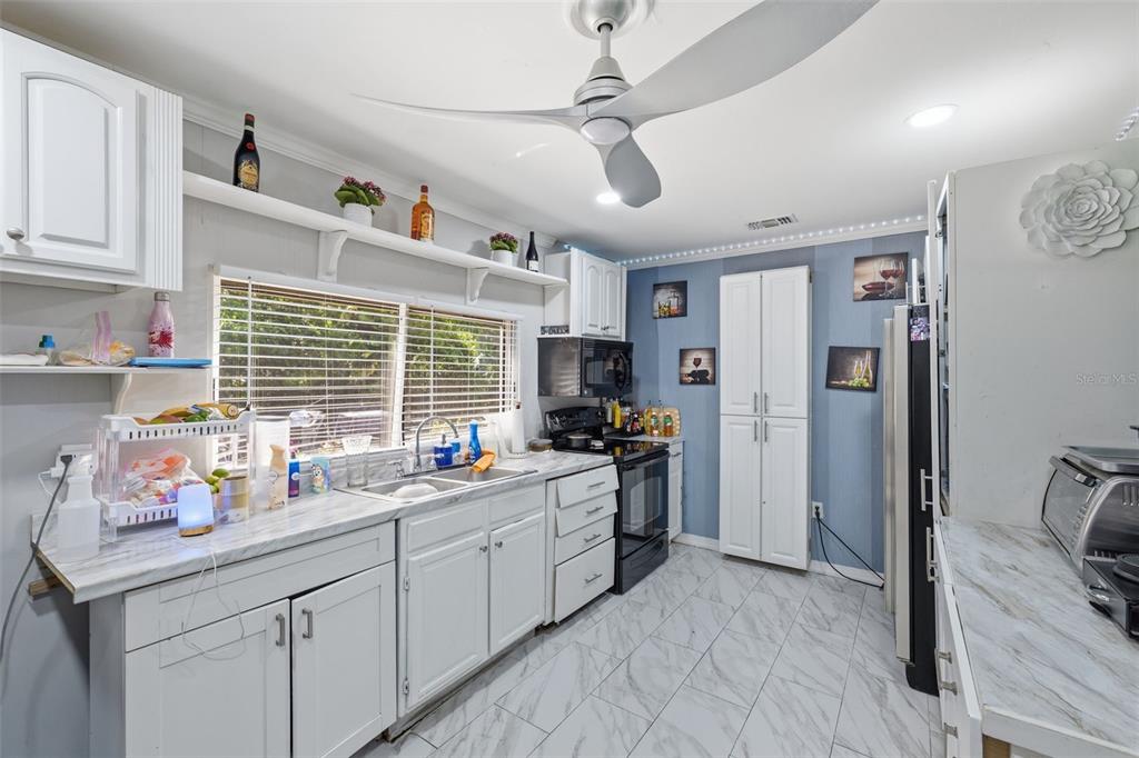 A kitchen features white cabinets, marble-look countertops, blue walls, and a ceiling fan — 2706 E ANNIE STREET, TAMPA, FL