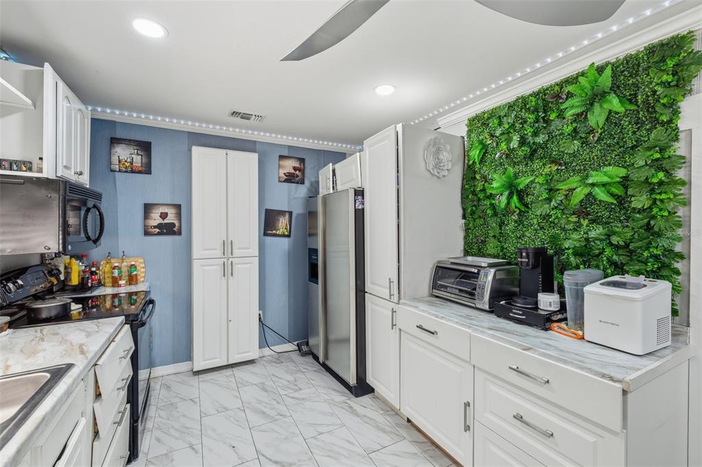 A kitchen features white cabinets, marble-look countertops, blue wallpaper, and a decorative green plant wall — 2706 E ANNIE STREET, TAMPA, FL
