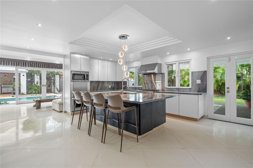 A modern kitchen features a large dark island, white cabinetry, and glass doors opening outdoors — 18 PASEO LAS PALMAS, DORADO, PR, PR