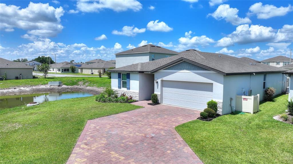 A single-story house with a two-car garage, brick paver driveway, and a small pond — 1355 BENEVENTO DRIVE, WINTER HAVEN, FL