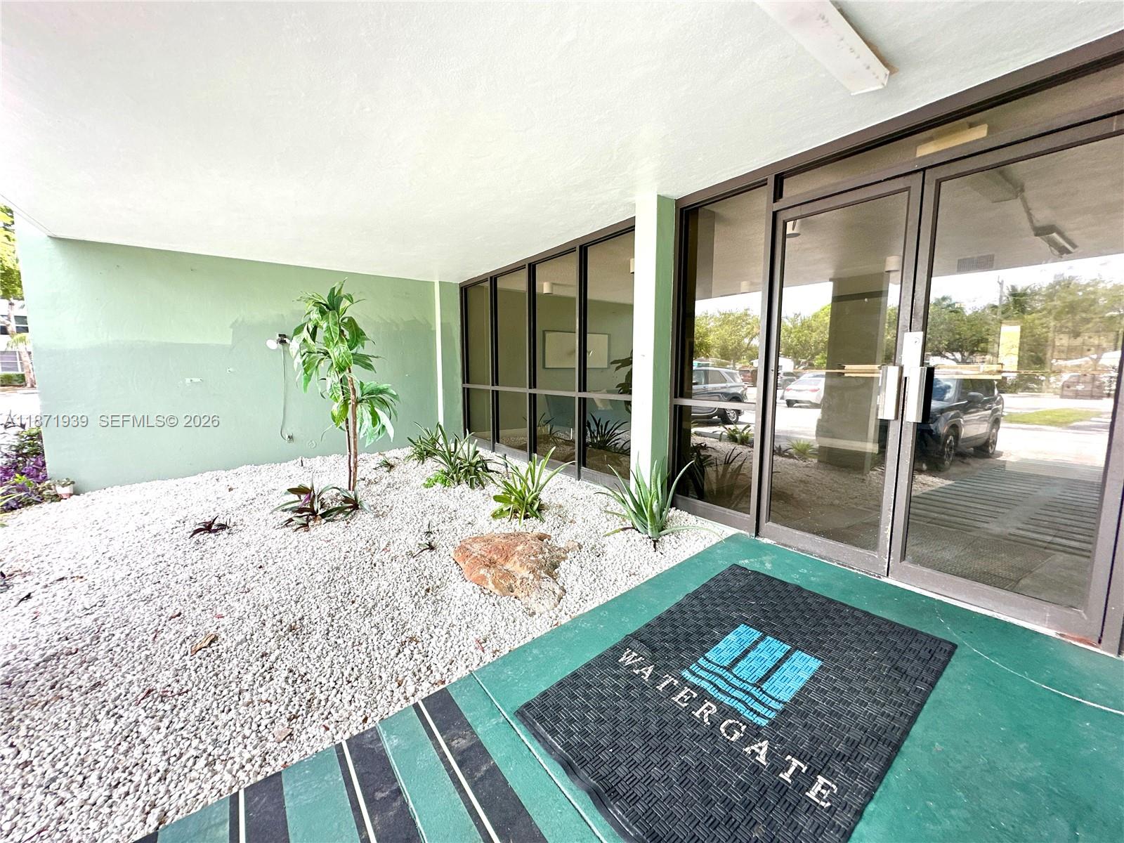 The entrance to the Watergate building features a glass door, a logo mat, and gravel landscaping — 2771 Taft St # 302, Hollywood FL 33020, HOLLYWOOD, FL