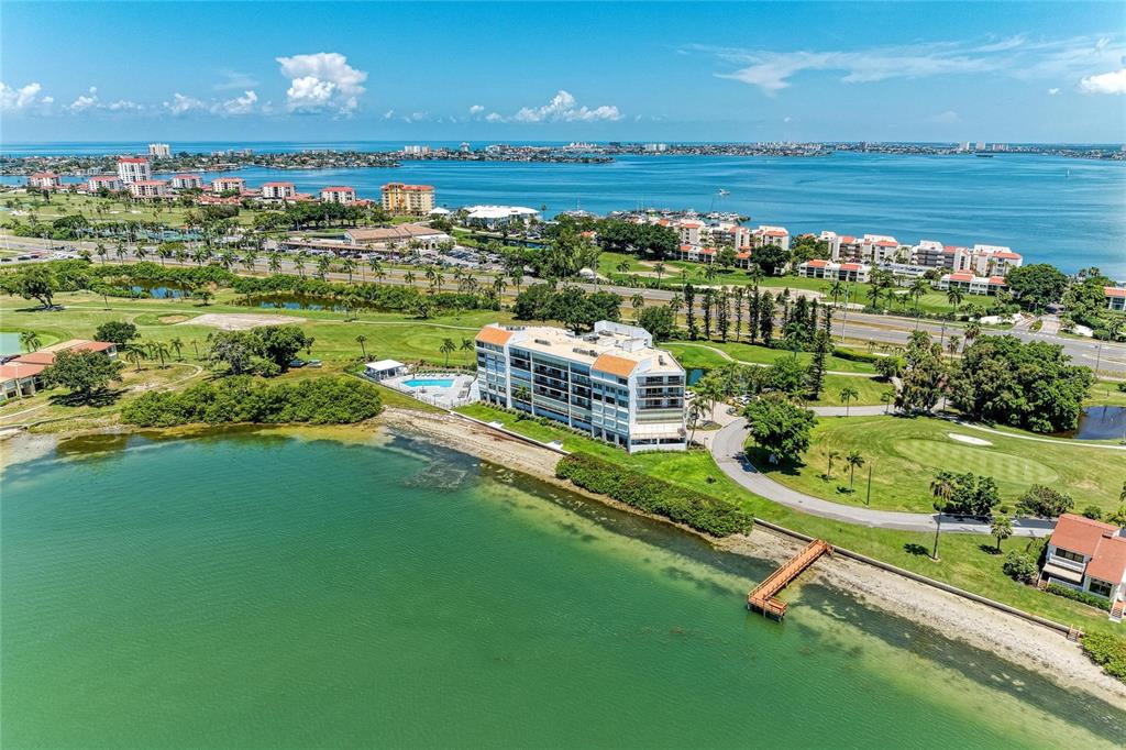 An aerial view shows a multi-story apartment building situated on a waterfront golf course — 5700 ESCONDIDA BOULEVARD S UNIT 506, ST PETERSBURG, FL
