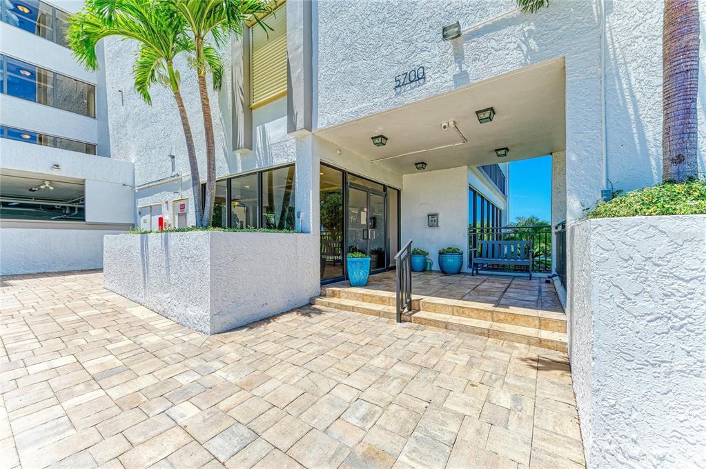 The exterior entrance of a building features a paved patio, palm trees, and glass doors — 5700 ESCONDIDA BOULEVARD S UNIT 506, ST PETERSBURG, FL