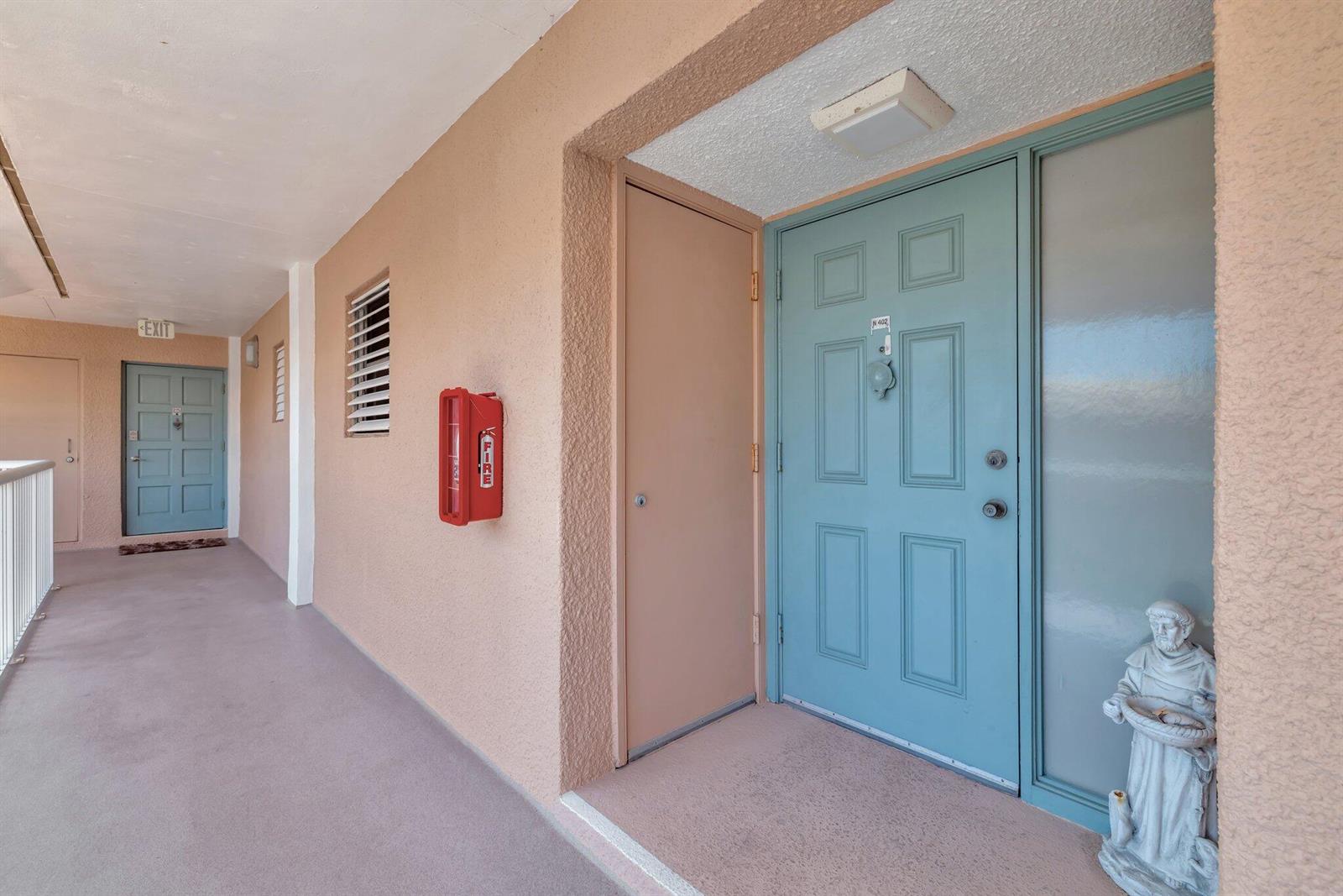 An exterior apartment hallway features peach-colored walls, blue doors, and a red fire extinguisher cabinet — 1555 NE Ocean Boulevard # 402, Stuart FL 34996, STUART, FL