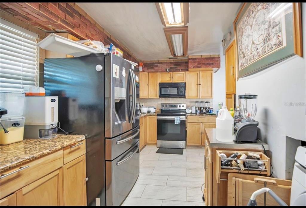 A kitchen with light wood cabinets, stainless steel appliances, granite countertops, and brick wall accents — 5108 FIGWOOD LANE, ORLANDO, FL