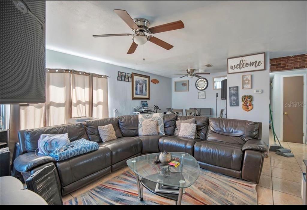 A living room features a large brown leather sectional, a glass coffee table, and ceiling fans — 5108 FIGWOOD LANE, ORLANDO, FL