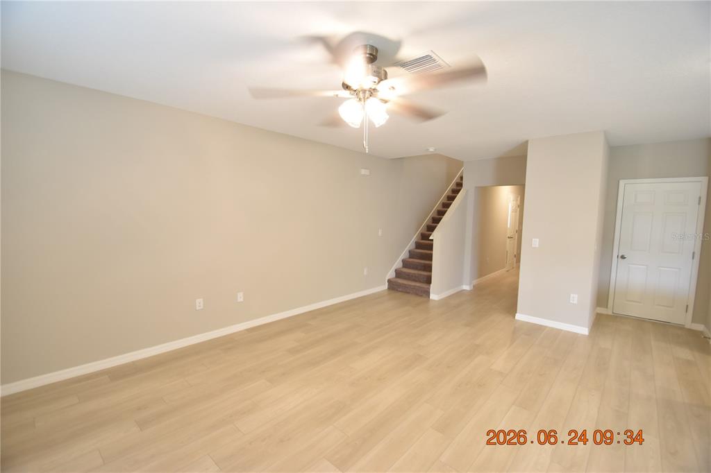 A living room with light wood-look flooring, a ceiling fan, and stairs leading upward — 14468 MEADOW BIRD AVENUE, RIVERVIEW, FL