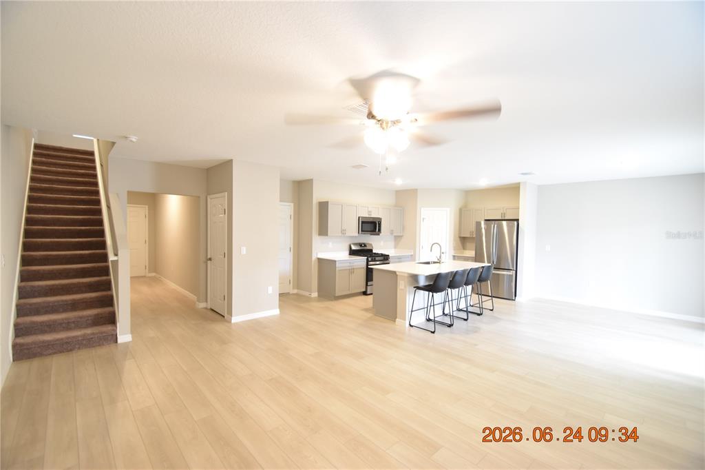 An open-concept kitchen and living area features light wood flooring and a carpeted staircase — 14468 MEADOW BIRD AVENUE, RIVERVIEW, FL