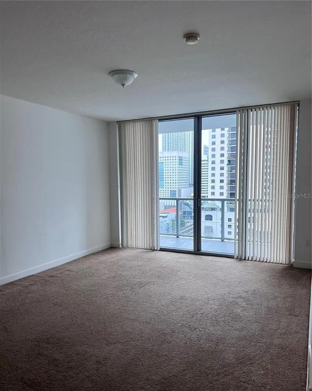 An empty room with brown carpet, white walls, and a balcony overlooking a city skyline — 1111 SW 1ST AVENUE UNIT 1924, MIAMI, FL