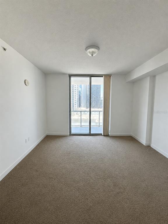 An empty room with beige carpet, white walls, and a sliding glass door to a balcony — 1111 SW 1ST AVENUE UNIT 1924, MIAMI, FL