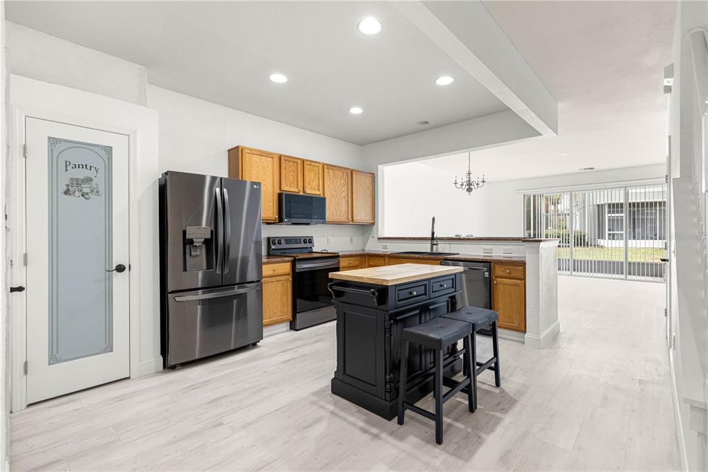 A kitchen features wood cabinets, stainless steel appliances, a black island, and a pantry door — 4131 SW 51ST CIRCLE, OCALA, FL