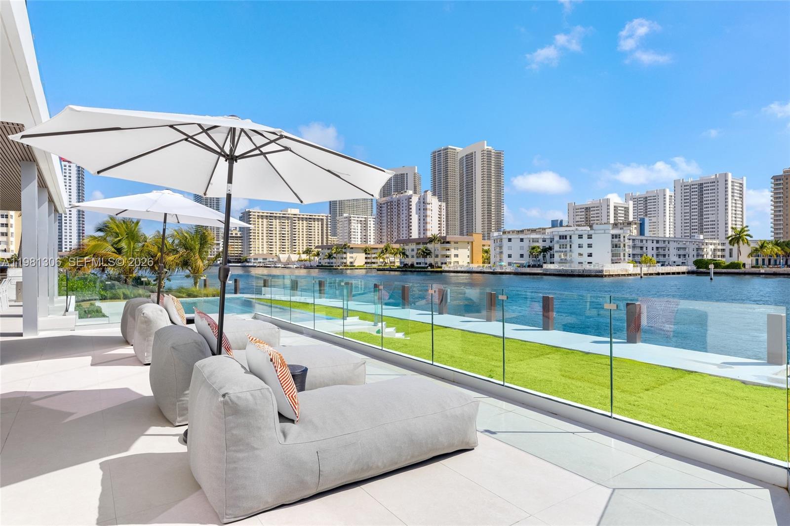 A patio with lounge chairs and umbrellas overlooks a waterway and city skyline — 503 Palm Dr, Hallandale Beach FL 33009, HALLANDALE BEACH, FL