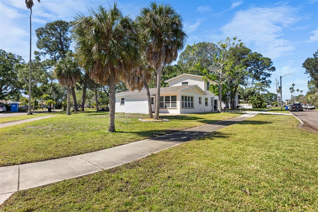 A white two-story house with a sunroom stands on a grassy lot with palm trees — 4038 HARRISBURG, ST PETERSBURG, FL