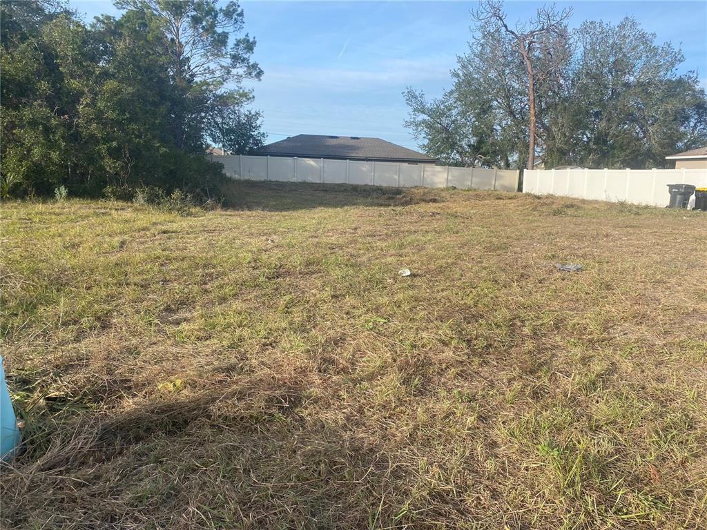 A vacant, grassy lot is enclosed by a white vinyl fence with trees in the background — 308 HIBISCUS DRIVE, POINCIANA, FL