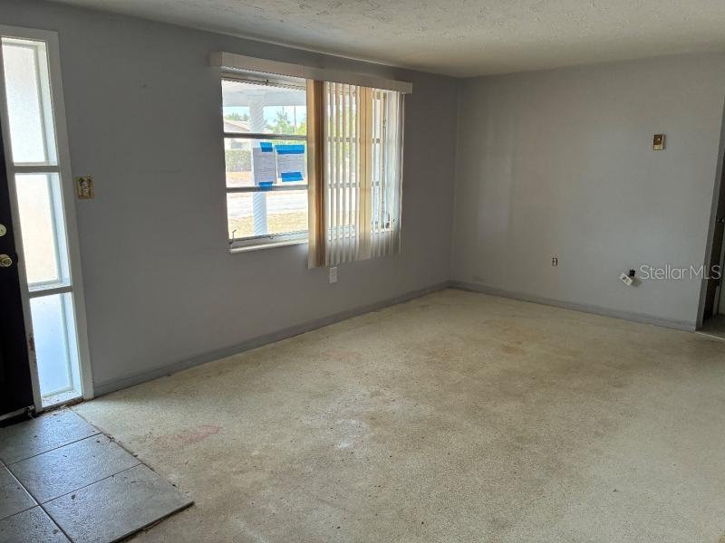 An empty room features light gray walls, a window with vertical blinds, and stained carpeting — 4816 PANORAMA AVENUE, HOLIDAY, FL