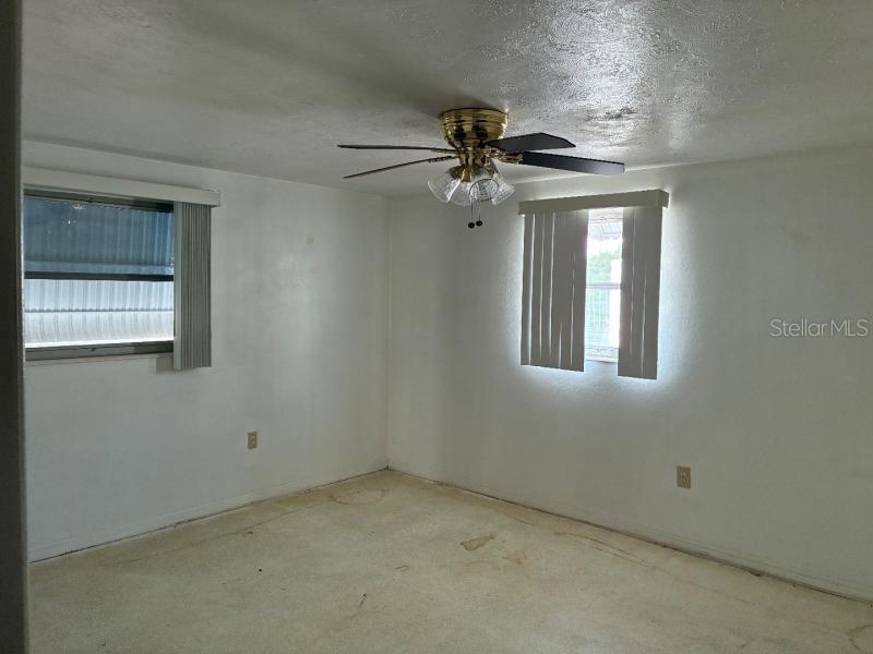 An empty bedroom features white walls, beige carpeting, a ceiling fan, and two windows — 4816 PANORAMA AVENUE, HOLIDAY, FL