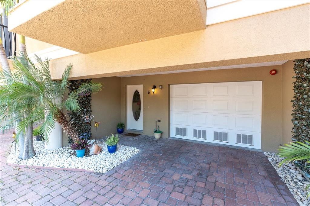 The exterior of a home features a white garage door, a front door, and landscaping — 300 CAPRI BOULEVARD UNIT 6, TREASURE ISLAND, FL