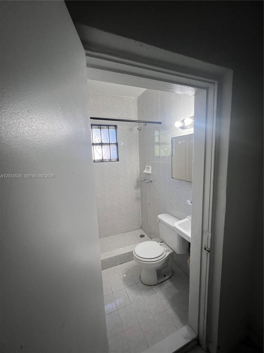 A small bathroom features light-colored wall and floor tiles, a toilet, and a walk-in shower — 1060 NW 116th St # 4, Miami FL 33168, MIAMI, FL
