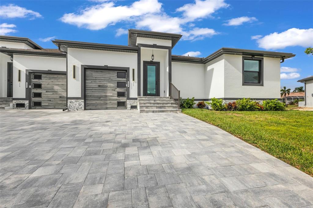 A modern single-story house features a paved driveway, wood-look garage doors, and white stucco walls — 1327 WESLEY DRIVE, PUNTA GORDA, FL