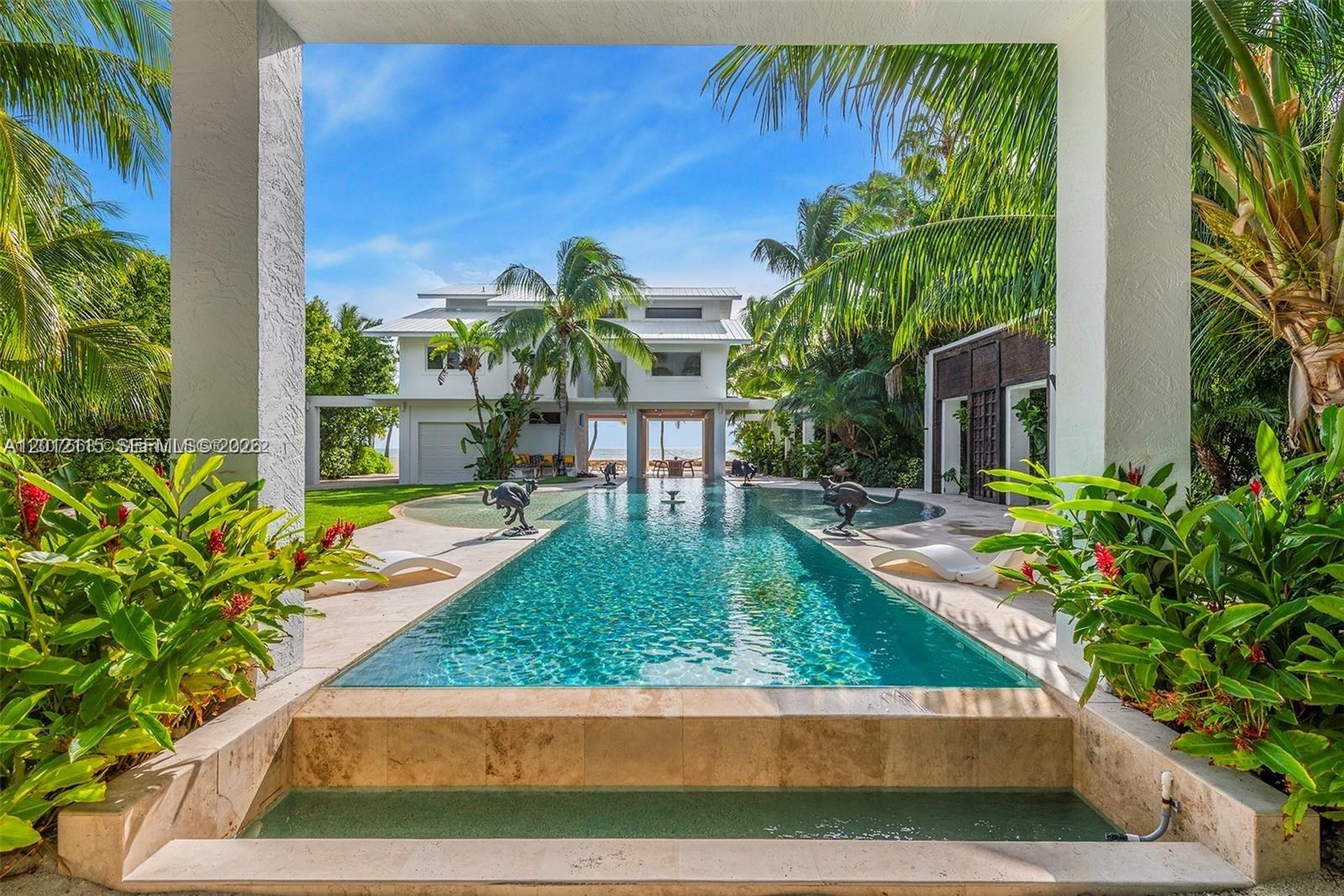 A long swimming pool sits between a white house and a covered patio area — 60 Ocean Front Dr, Key Largo FL 33037, KEY LARGO, FL