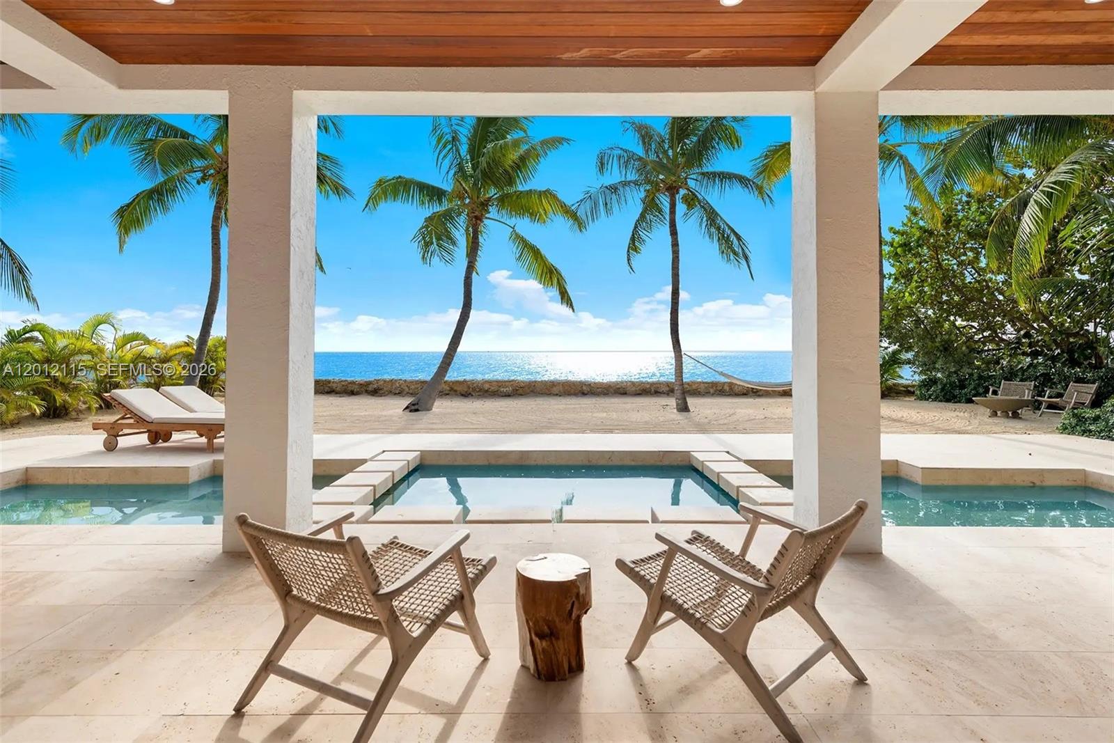 A covered patio features two chairs, a small wooden table, and a pool overlooking the ocean — 60 Ocean Front Dr, Key Largo FL 33037, KEY LARGO, FL