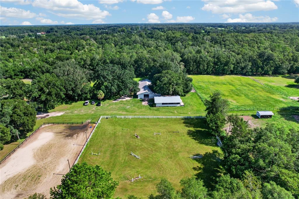 An aerial view shows a rural property with a barn, fenced pastures, and wooded surroundings — 9813 NW STATE ROAD 45, HIGH SPRINGS, FL