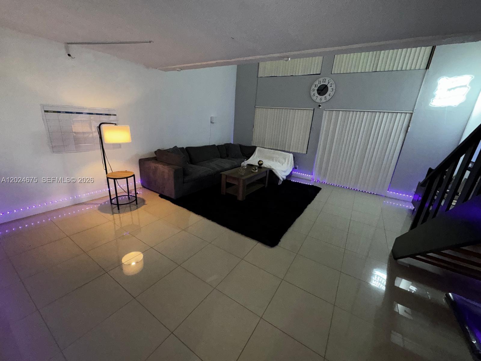 A living room features a dark sectional sofa, a black rug, and purple floor lighting — 18111 NW 68th Ave # F203, Hialeah FL 33015, HIALEAH, FL