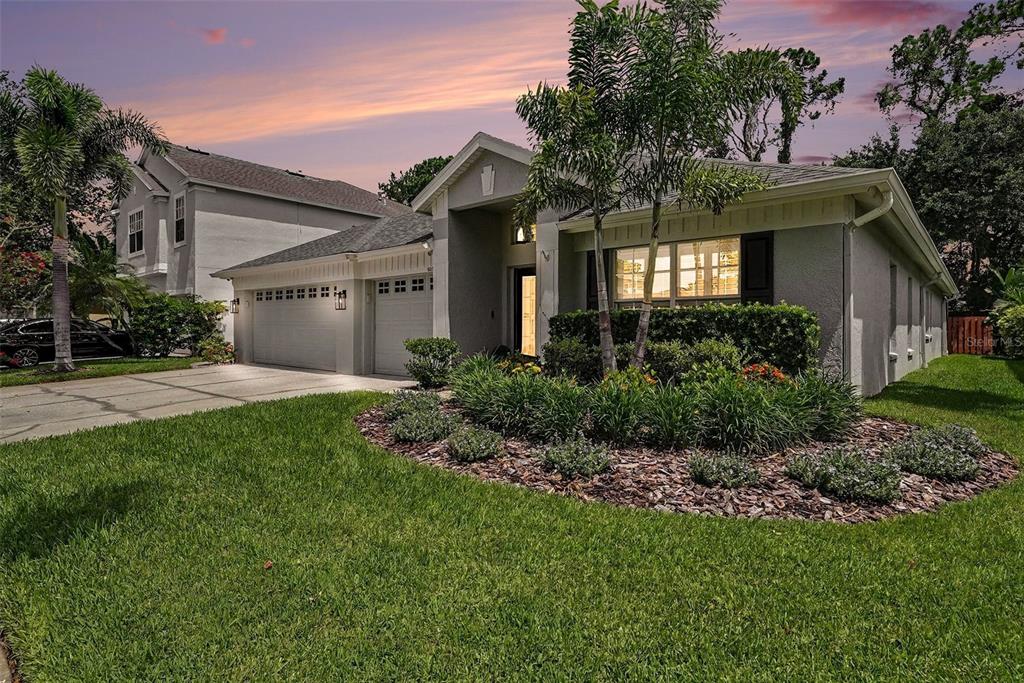 A single-story house with a two-car garage and a landscaped front yard at sunset — 10617 WEYBRIDGE DRIVE, TAMPA, FL