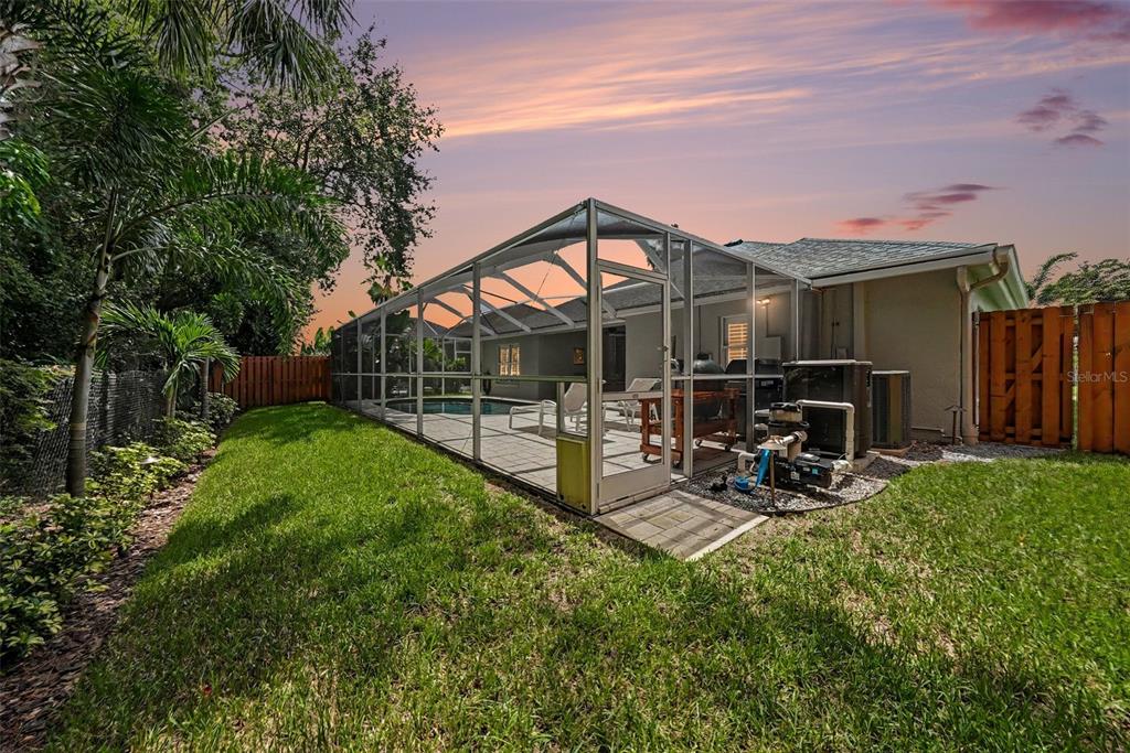 A backyard view of a house with a screened-in pool enclosure and a wooden fence — 10617 WEYBRIDGE DRIVE, TAMPA, FL
