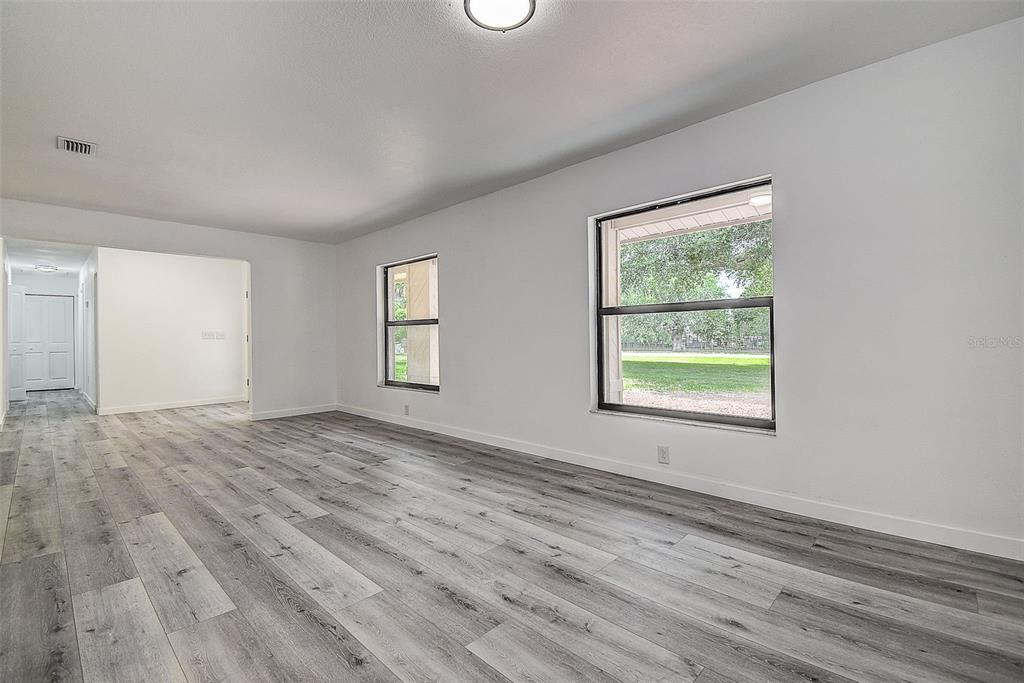A bright, empty room features gray wood-look flooring, white walls, and two large windows — 9404 W HAMILTON AVENUE, TAMPA, FL