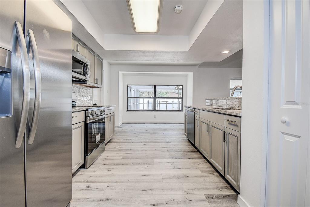 A kitchen with stainless steel appliances, light wood-look flooring, and gray cabinetry — 9404 W HAMILTON AVENUE, TAMPA, FL