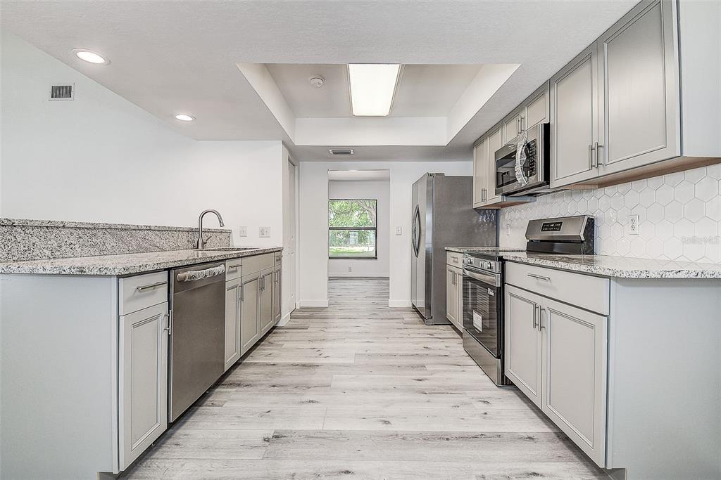 A modern kitchen features light gray cabinets, granite countertops, stainless steel appliances, and wood-look flooring — 9404 W HAMILTON AVENUE, TAMPA, FL