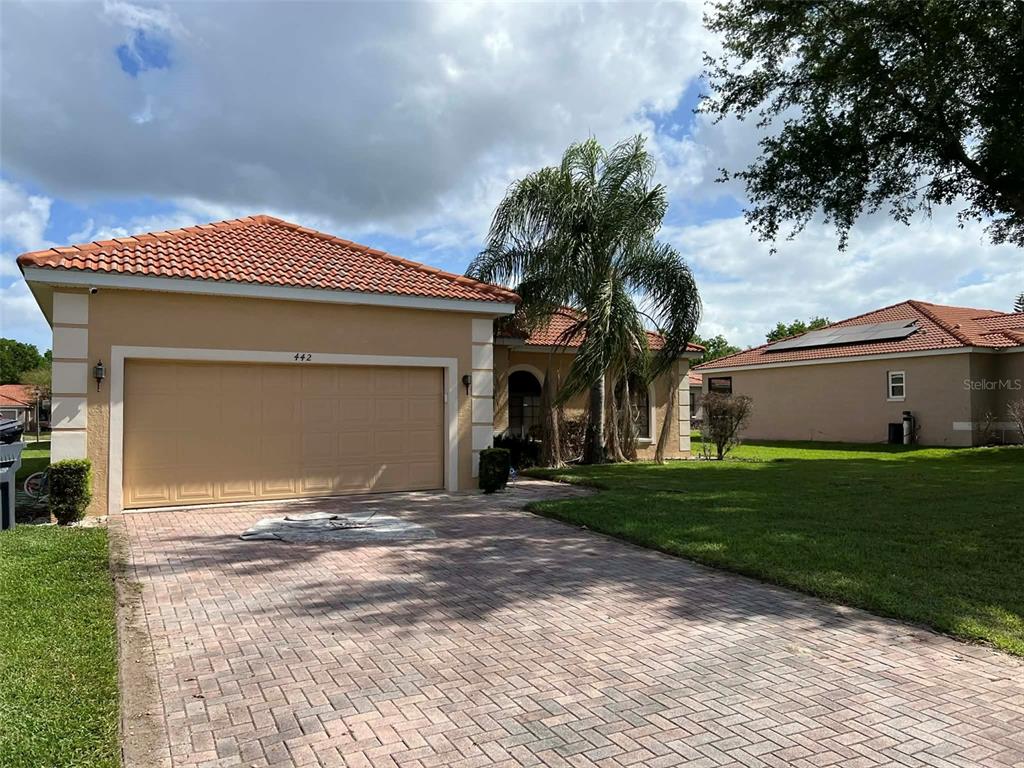 A single-story house with a tan exterior, a tiled roof, and a paved driveway — 442 CARAWAY DRIVE, KISSIMMEE, FL