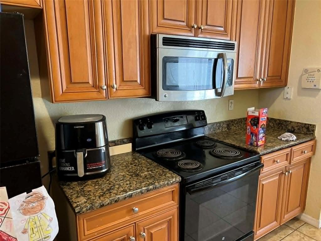 A kitchen features wood cabinets, granite countertops, a black electric stove, and a microwave — 442 CARAWAY DRIVE, KISSIMMEE, FL