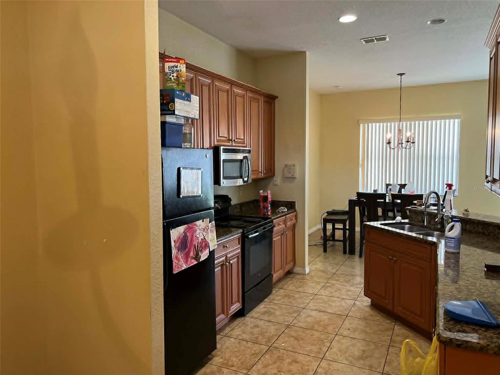 A kitchen with wood cabinets, black appliances, and a granite island overlooks a dining area — 442 CARAWAY DRIVE, KISSIMMEE, FL