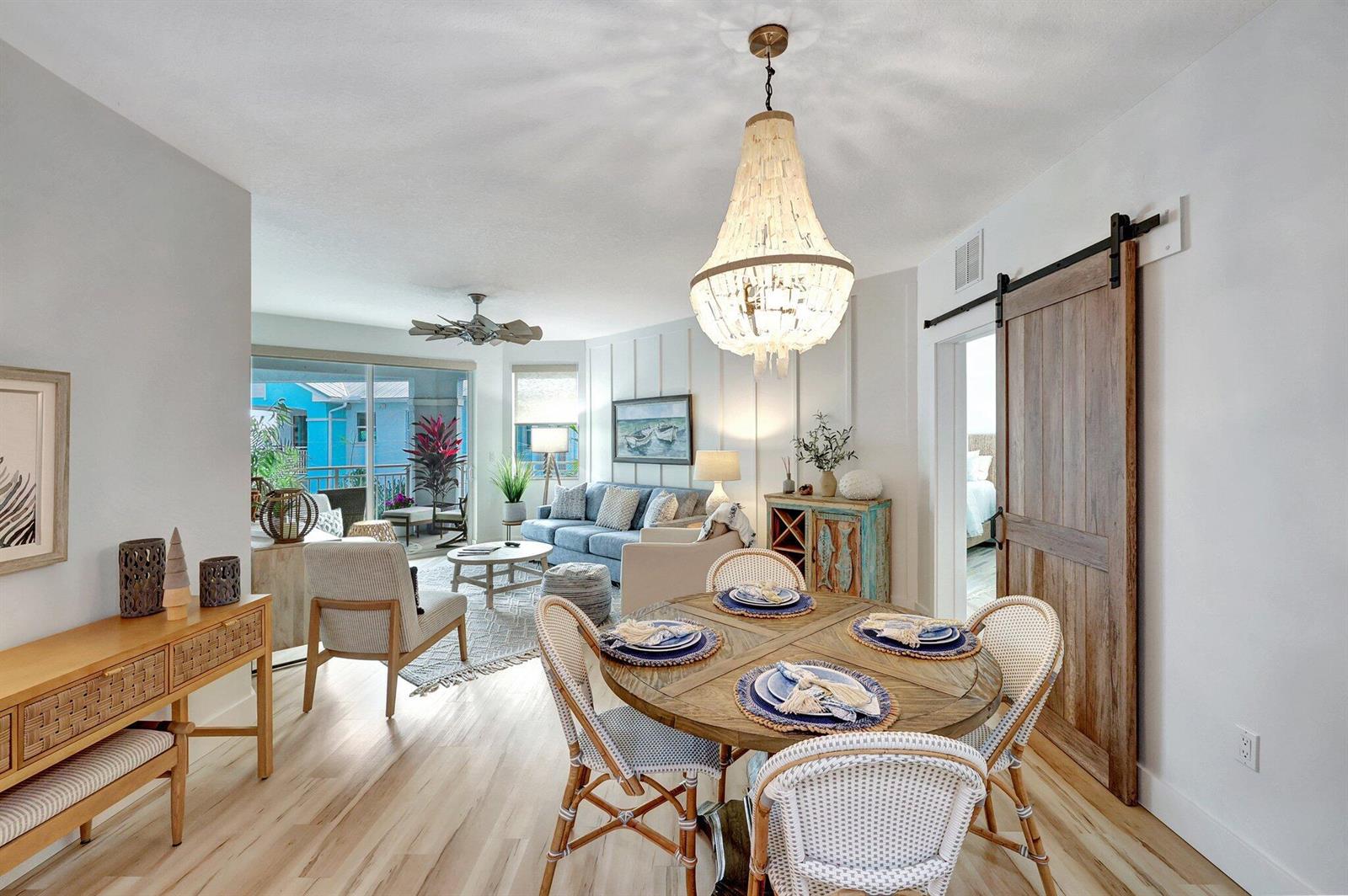 A dining area with a round wooden table sits before a living room and balcony — 875 NW Flagler Avenue # 404, Stuart FL 34994, STUART, FL