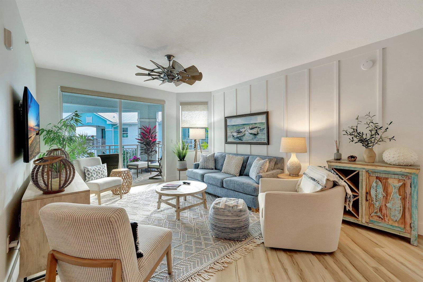 A coastal-style living room features a blue sofa, patterned rug, and a balcony view — 875 NW Flagler Avenue # 404, Stuart FL 34994, STUART, FL
